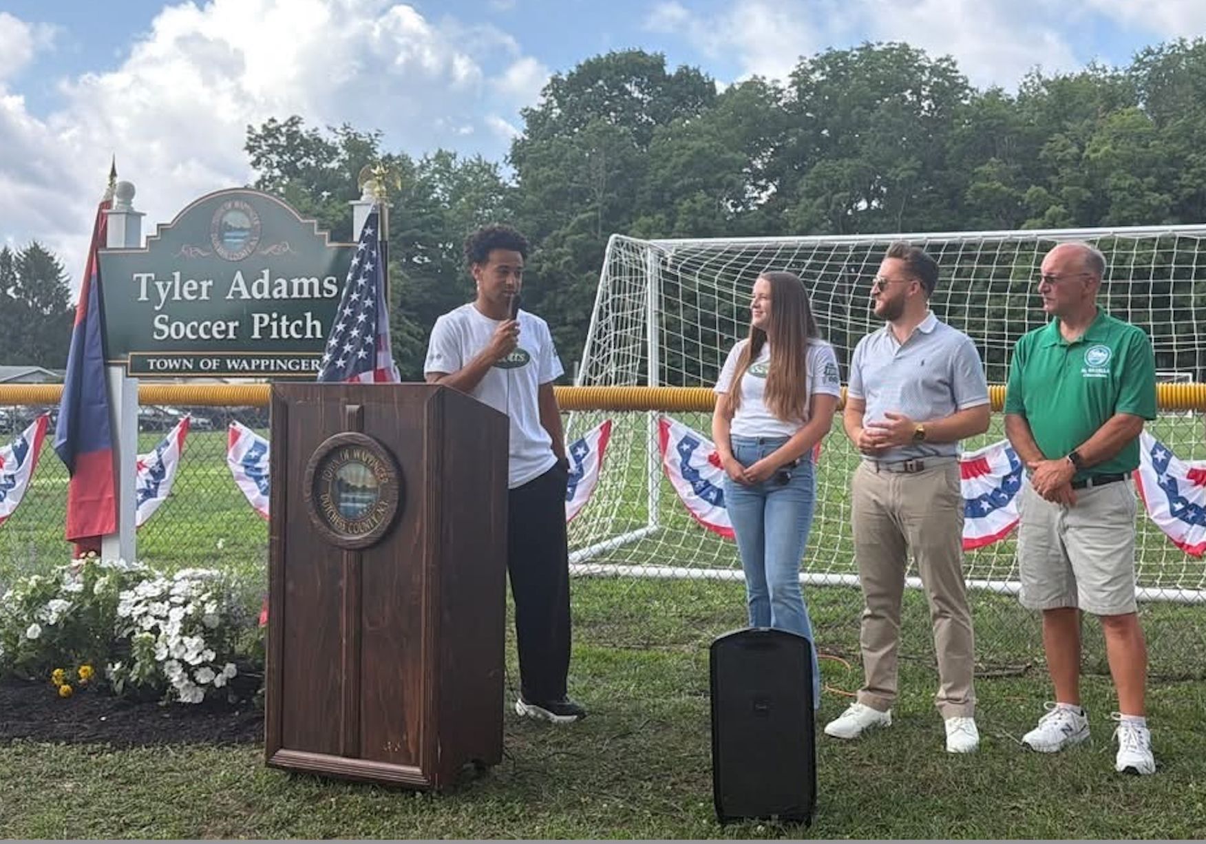 Speaker at podium during Tyler Adams Soccer Pitch dedication ceremony with three people standing nearby