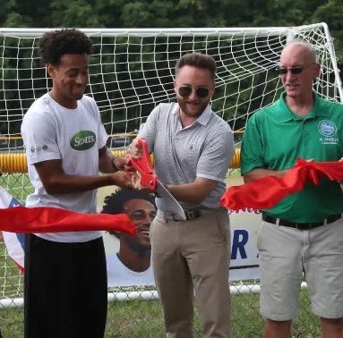 People cutting a red ribbon during an outdoor soccer field opening ceremony