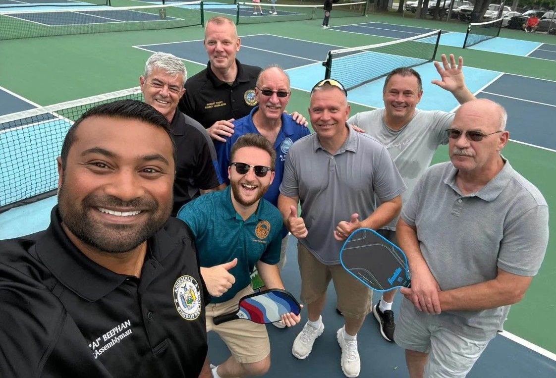 Group selfie of seven people holding pickleball paddles on an outdoor court