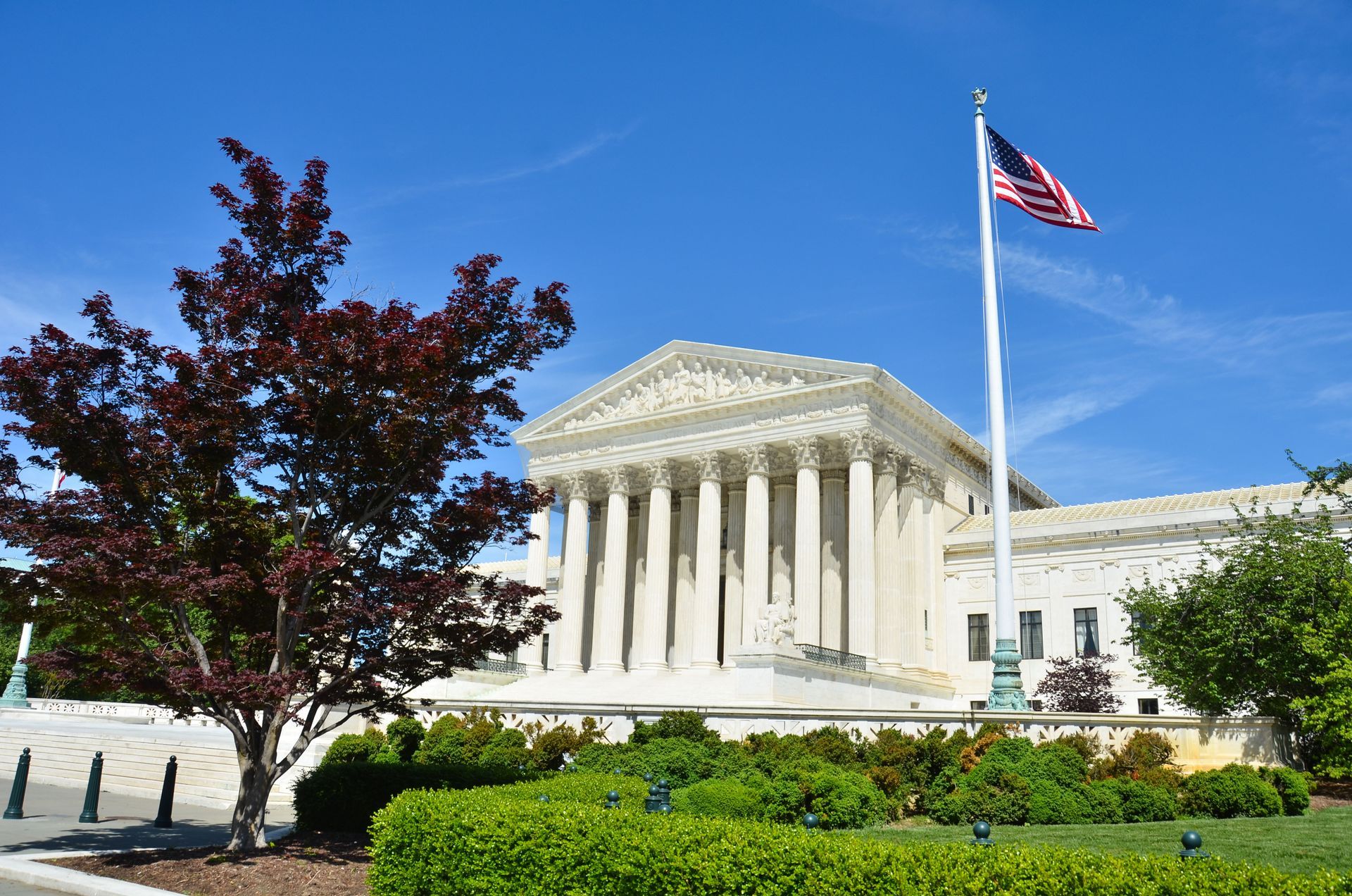 U.S. Supreme Court building with columns and an American flag against a blue sky