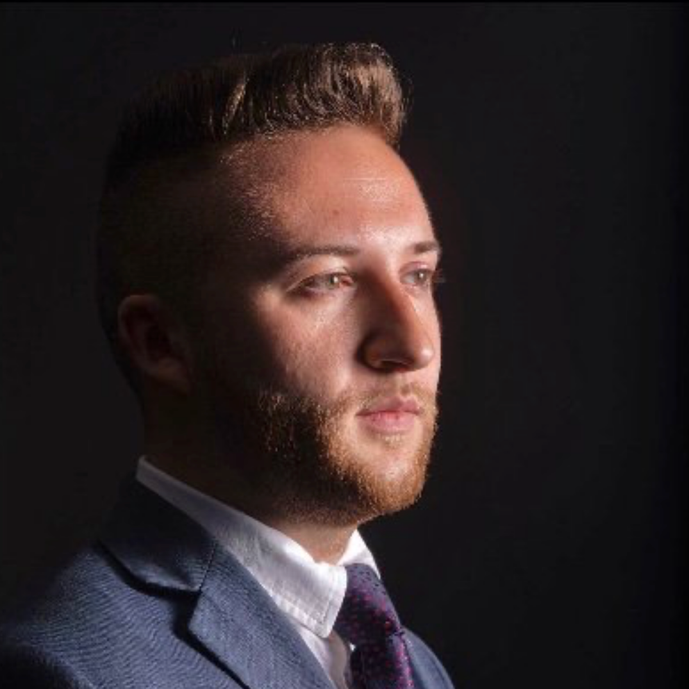 Portrait of a man in a suit, lit from the side against a dark background.