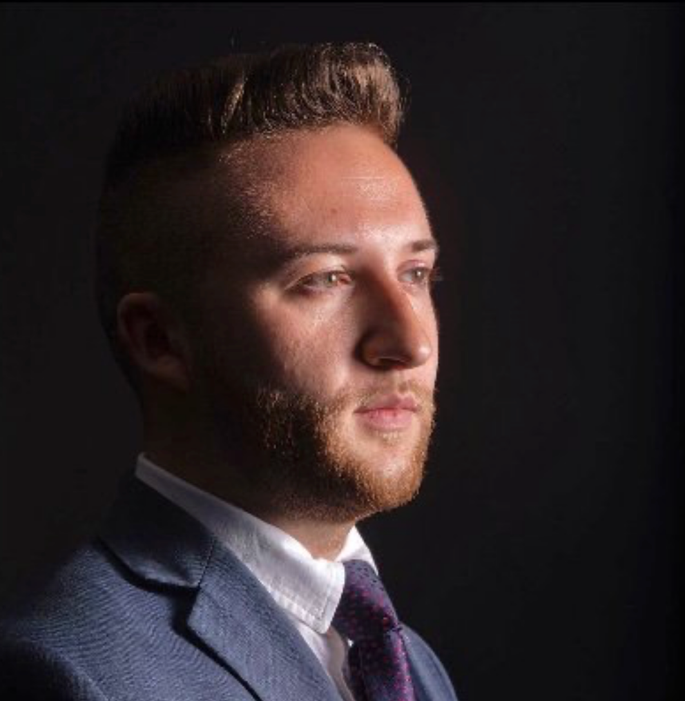 Portrait of a man in a suit, lit from the side against a dark background.