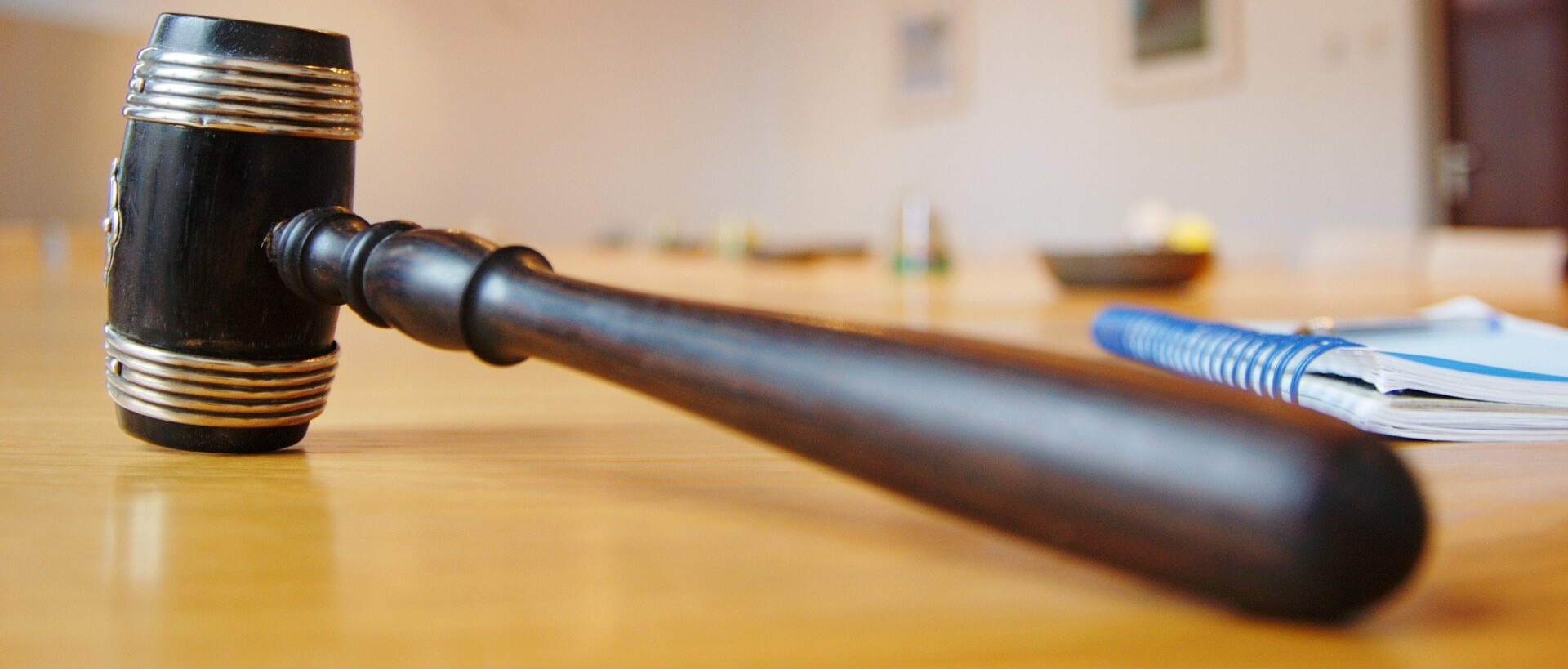 A wooden gavel on a light-colored table, likely in a meeting room or courtroom.