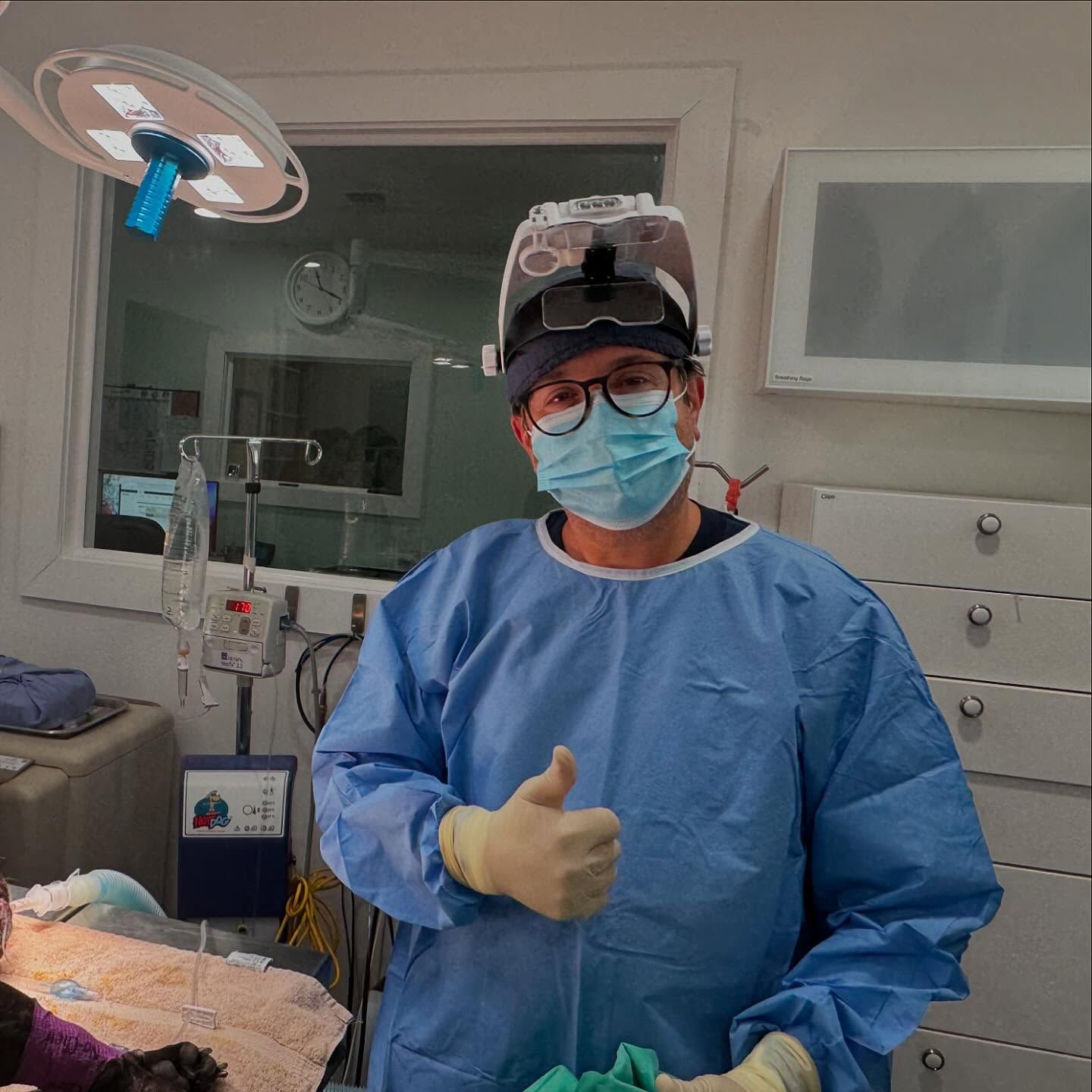 A surgeon wearing a mask and gown is giving a thumbs up