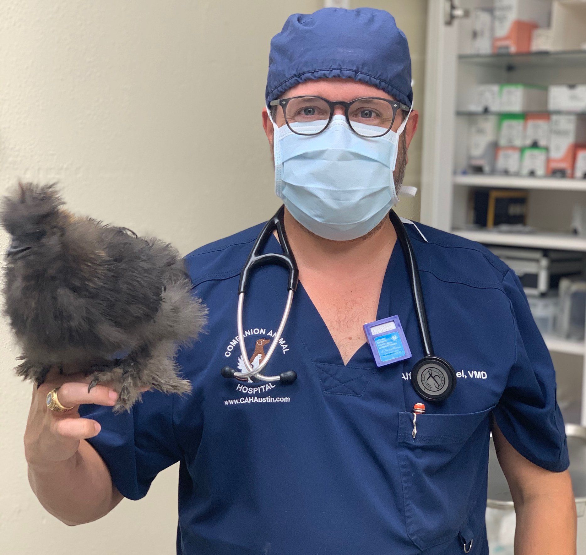 A man wearing a mask and scrubs is holding a cat