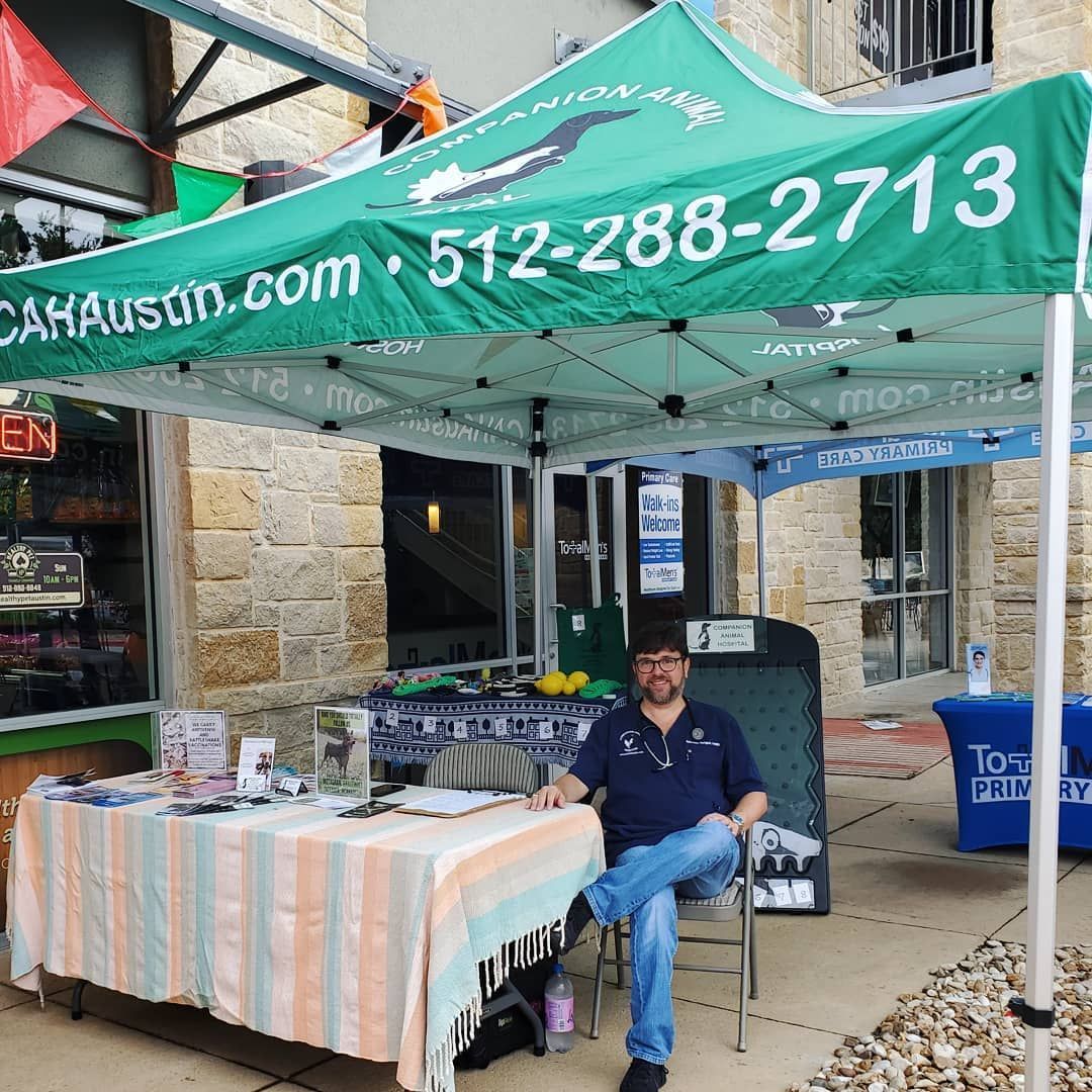 A man is sitting under a green canopy that says 512-288-2714