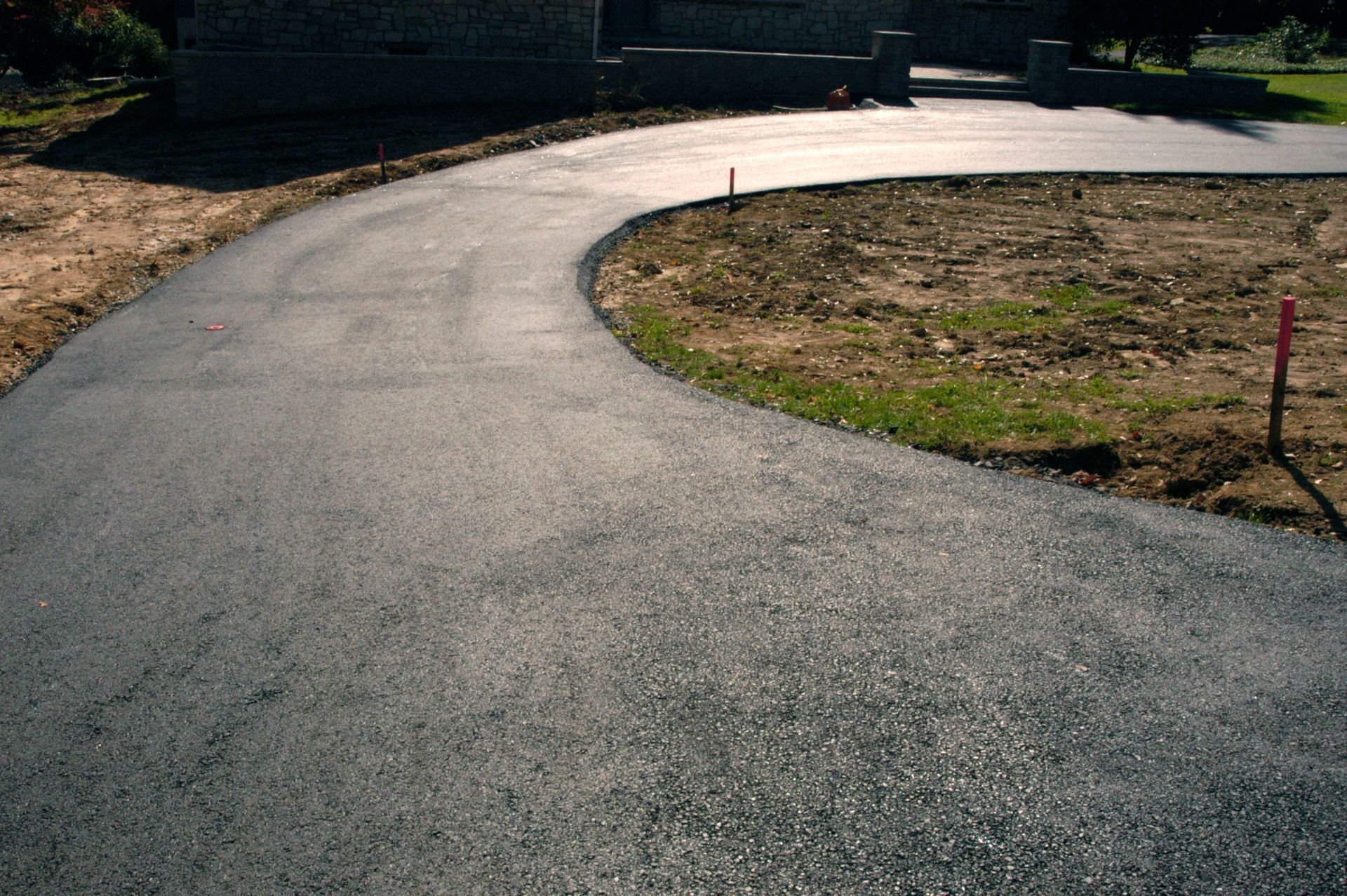 Curving asphalt driveway in front of a building; brown grass and soil on the sides.