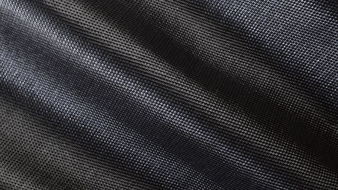 Close-up of a textured, woven black fabric, with subtle light reflections creating diagonal patterns.