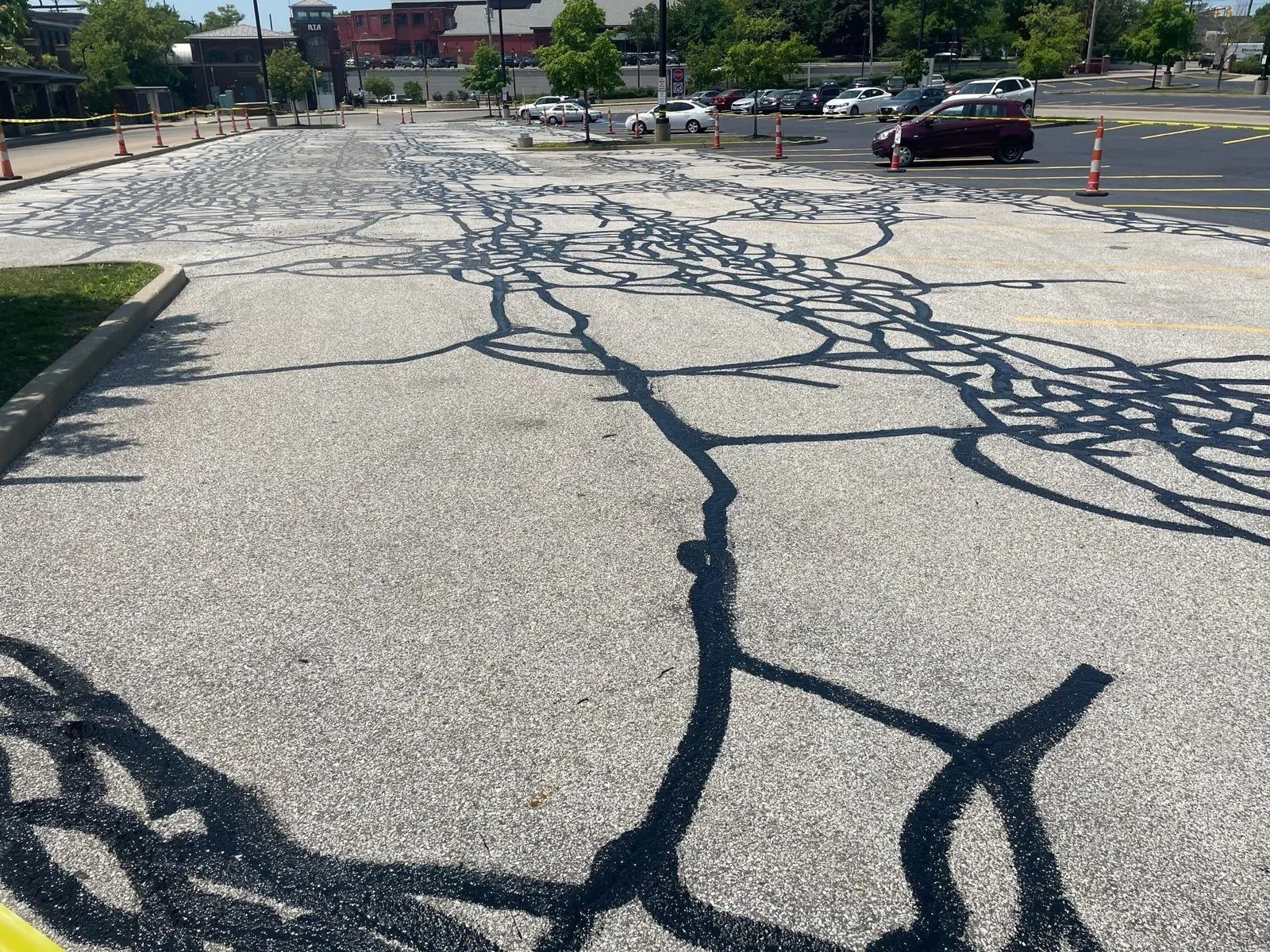 Asphalt parking lot with cracks sealed in black. Cars and a building are in the background.