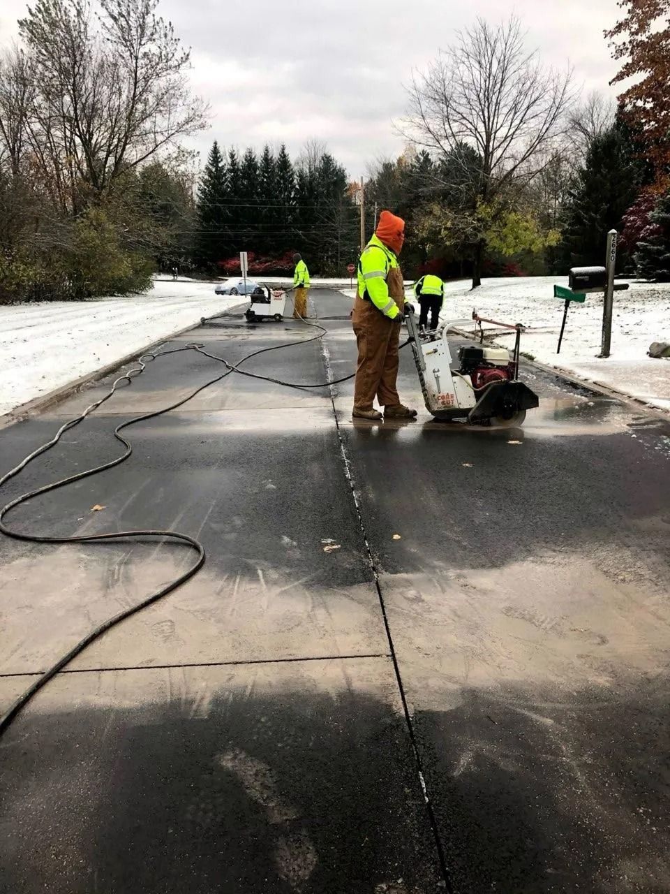 Road workers repairing asphalt pavement. Workers wearing safety vests and hard hats in an overcast setting.
