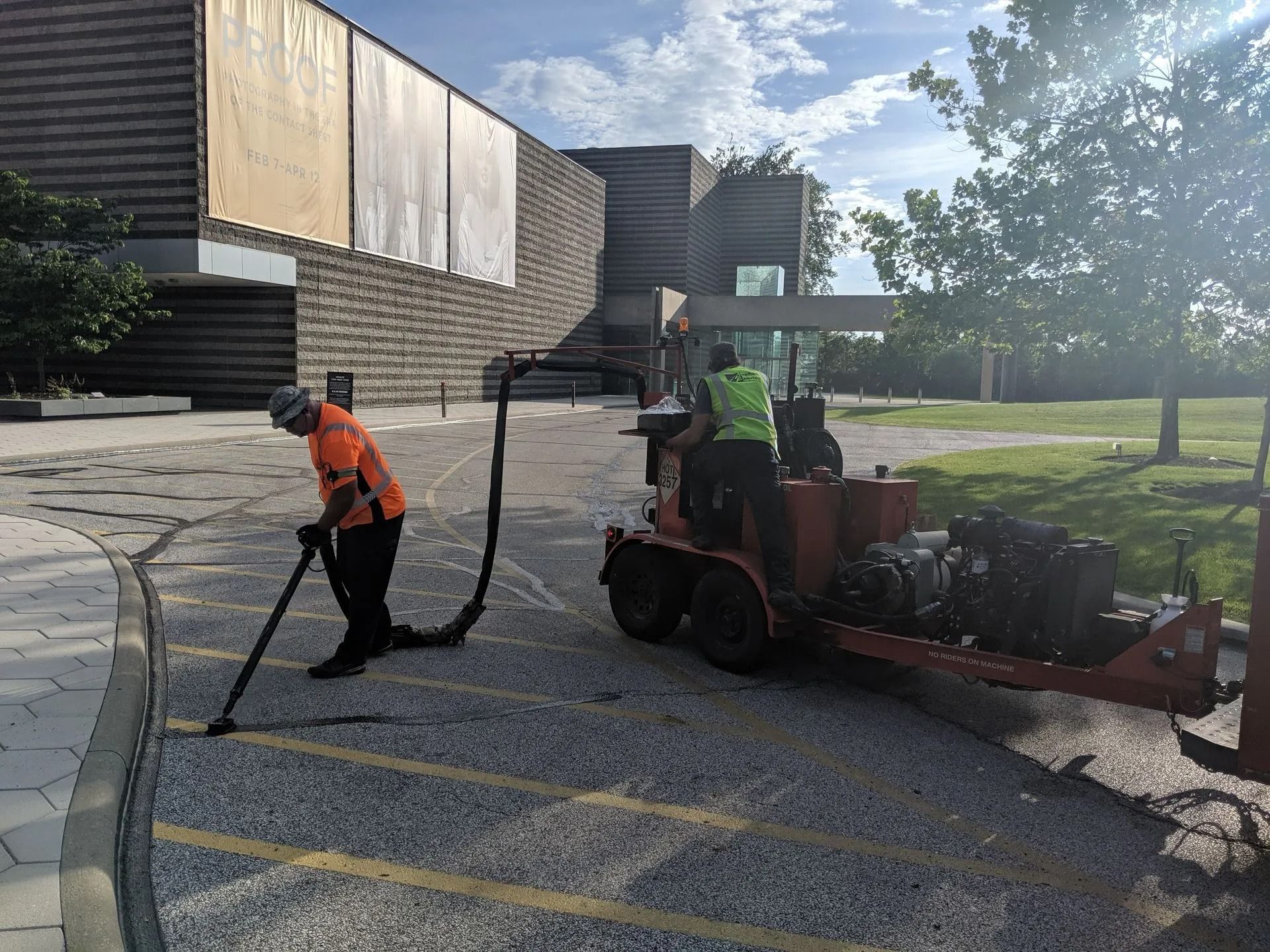Two workers use a machine to clean a parking area near a building.