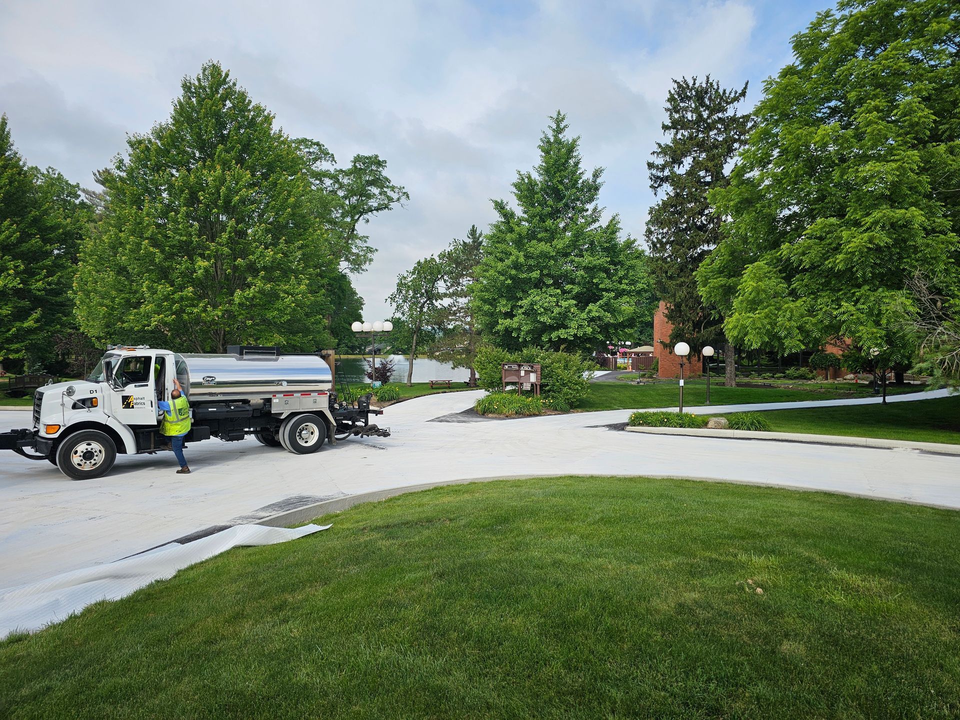 A white water truck spraying a white substance on a curved road in a park-like setting.