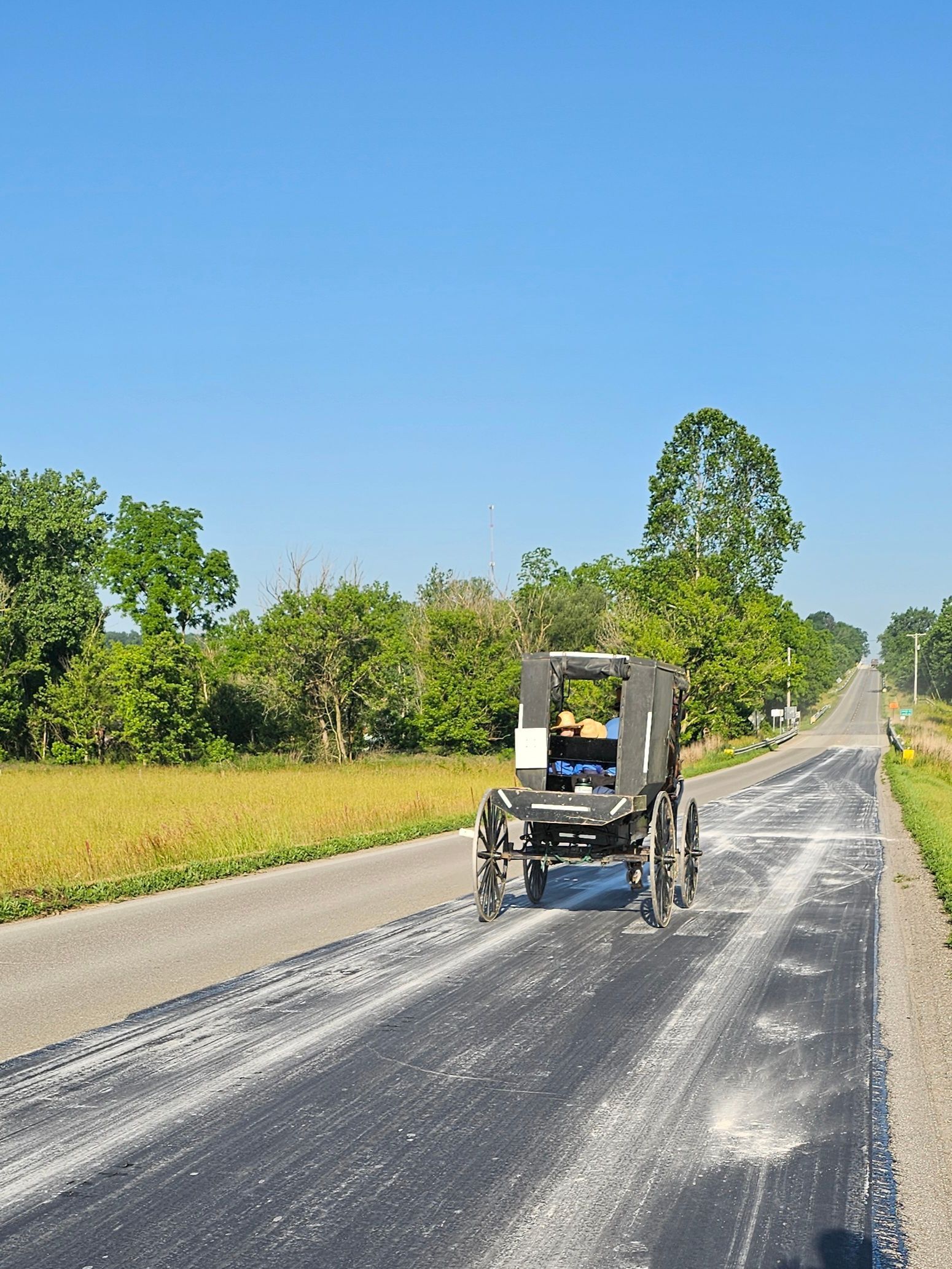 An Amish buggy on a freshly paved road, under a clear blue sky.