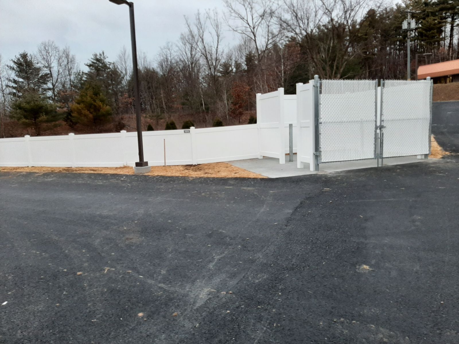 A white fence surrounds a lot with trees in the background