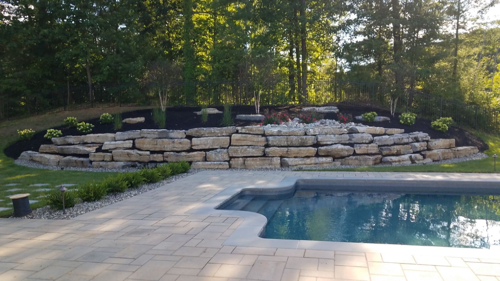A large stone wall surrounds a swimming pool in a backyard