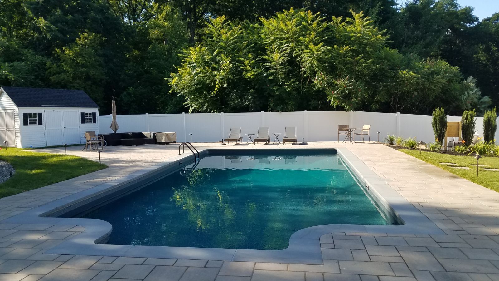 A large swimming pool is surrounded by a white fence