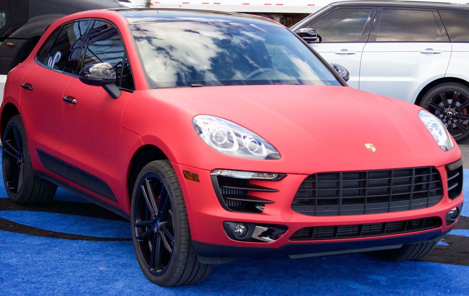 A red porsche macan is parked on a blue carpet