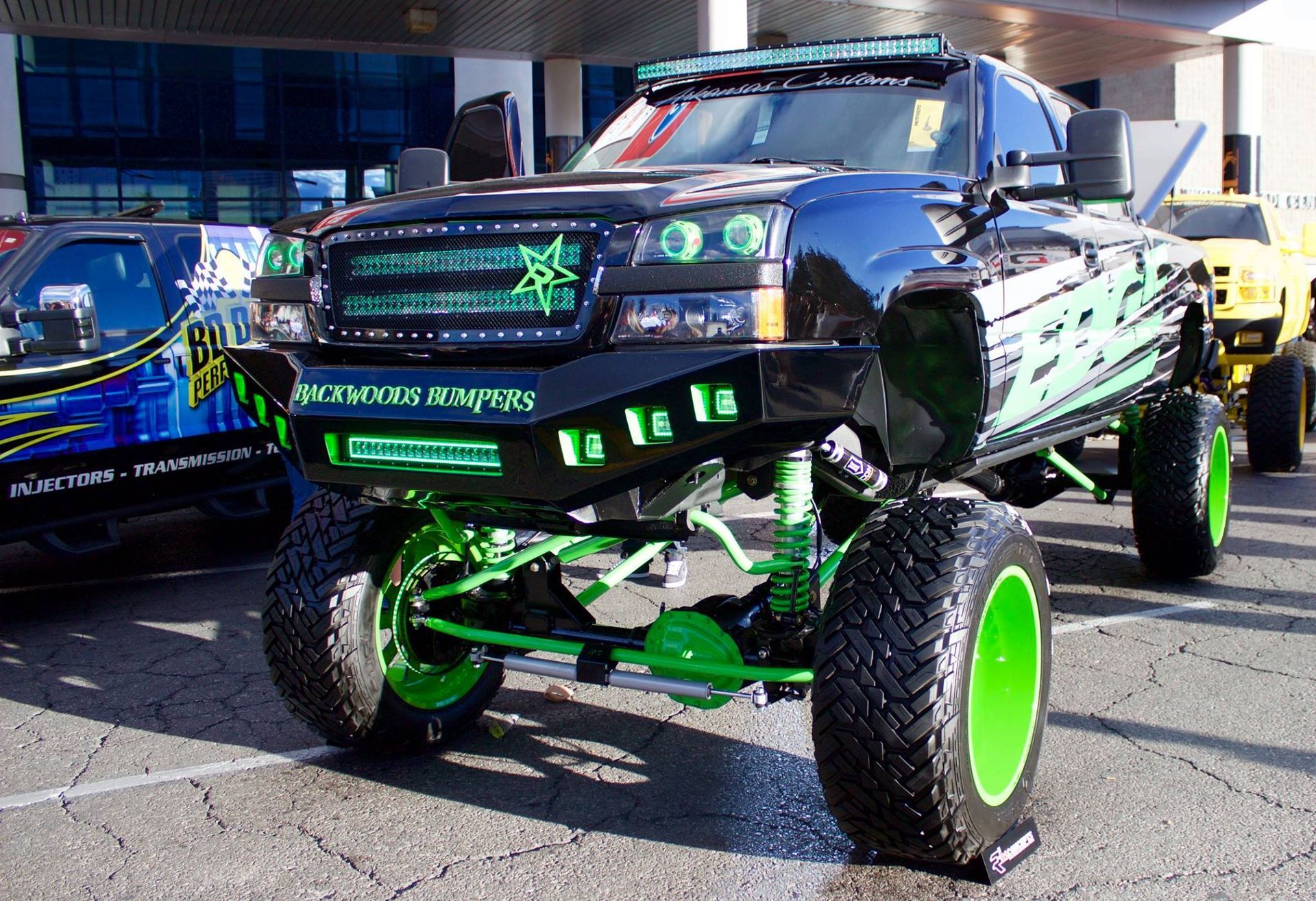 A black truck with green wheels is parked in a parking lot