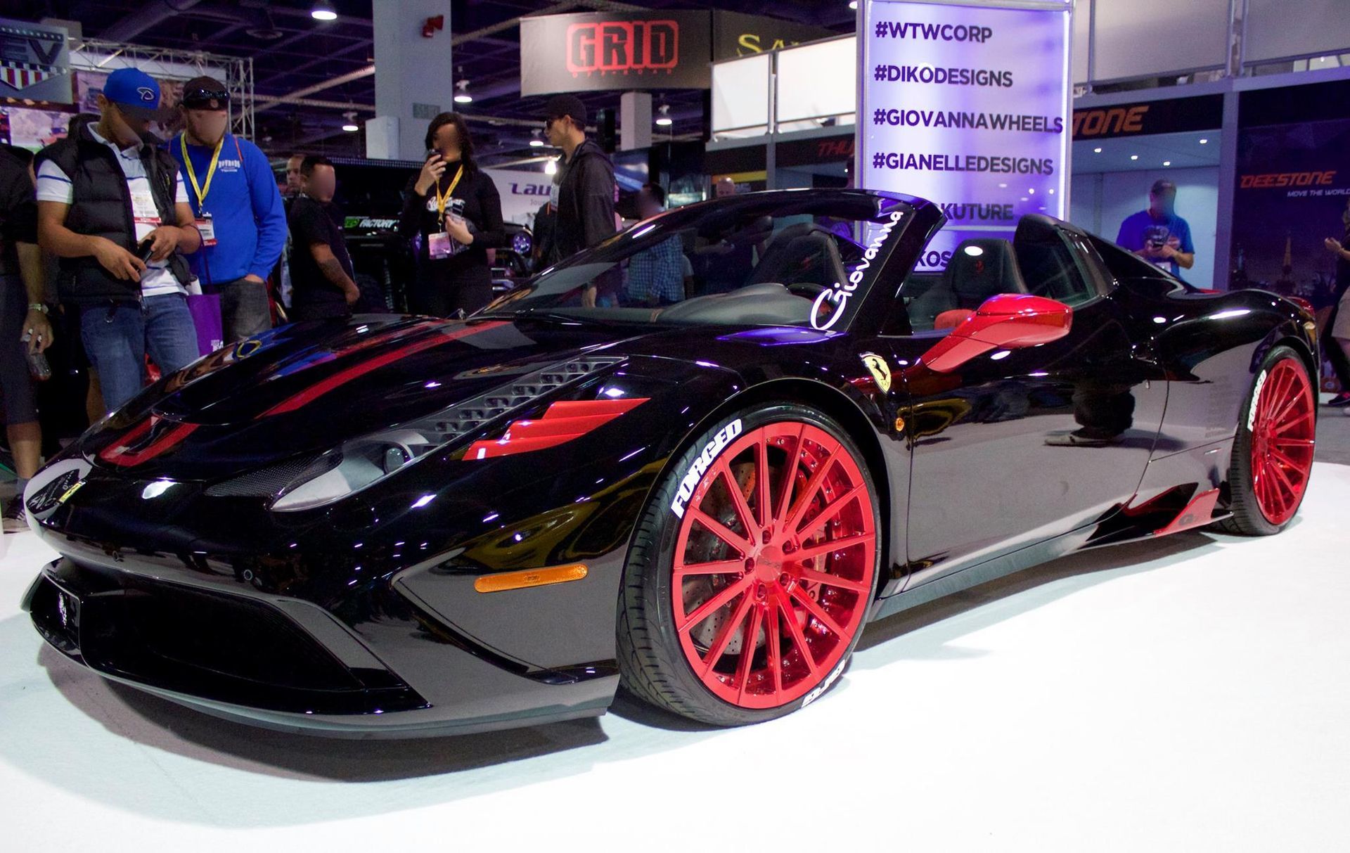 A black car with red wheels is on display at a car show