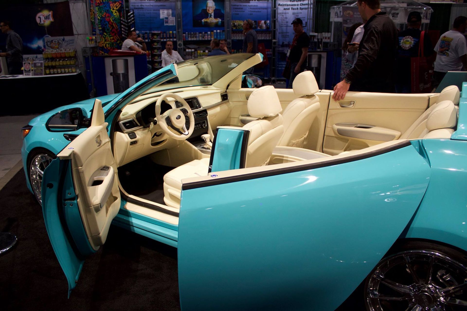 A blue car with the doors open is on display at a car show