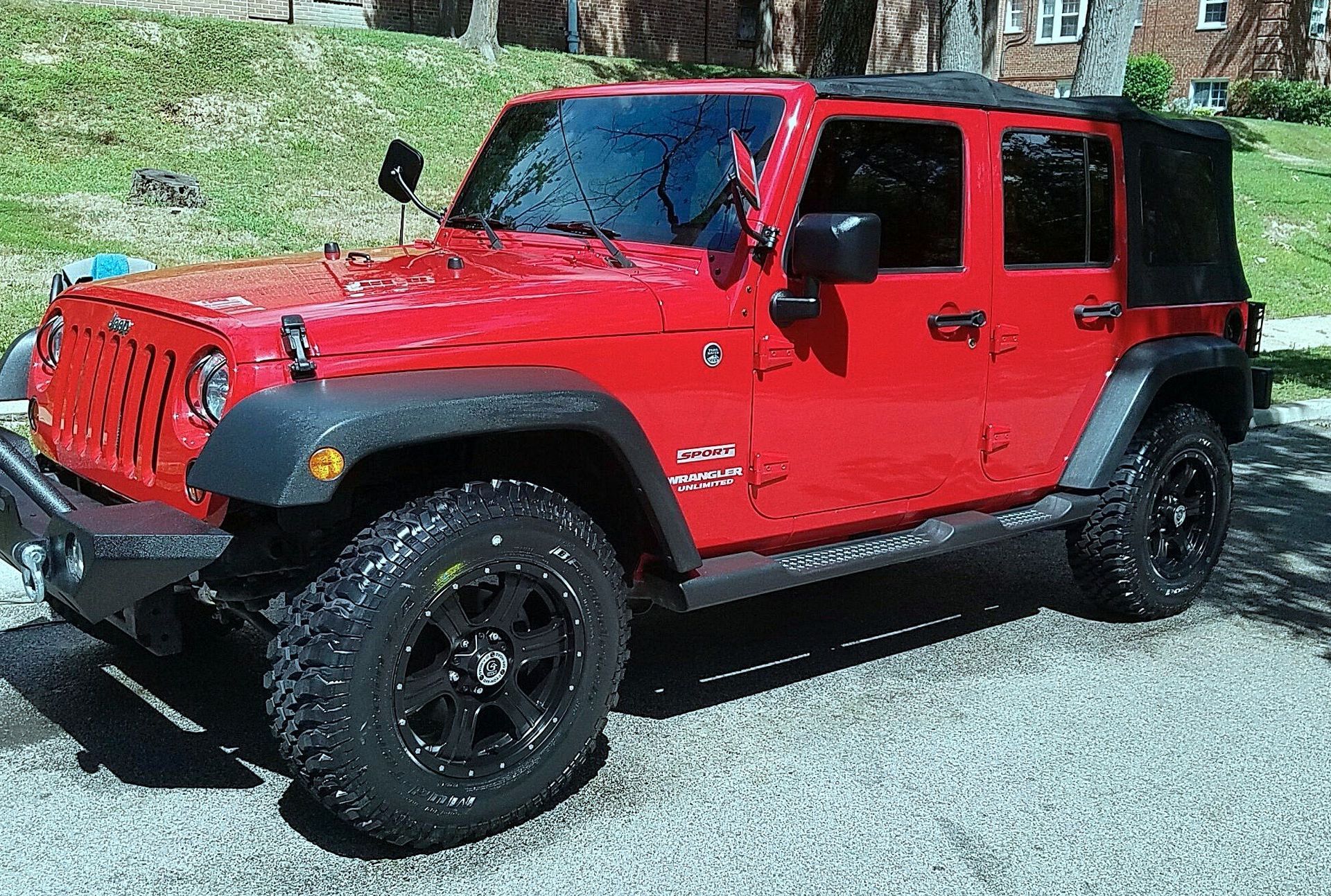 A red jeep is parked on gravel in front of a house.