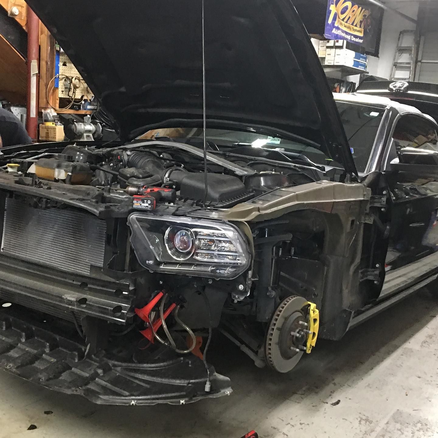 A car with the hood up is being worked on in a garage.