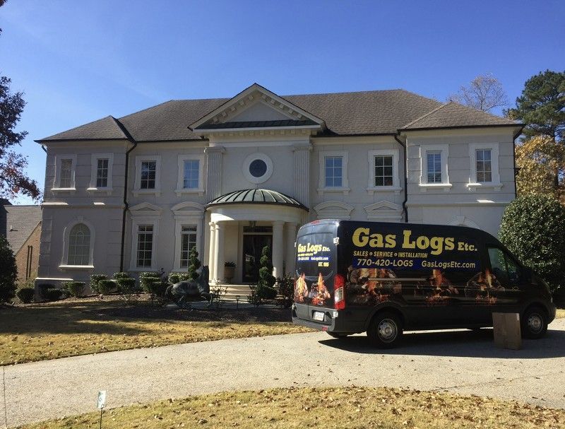 A gas logs van is parked in front of a large house