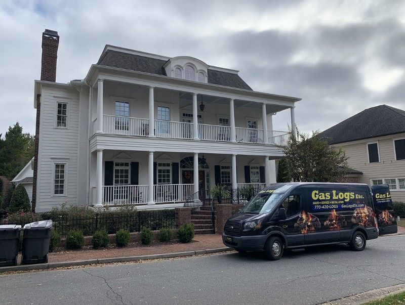 A gas logs van is parked in front of a large white house.