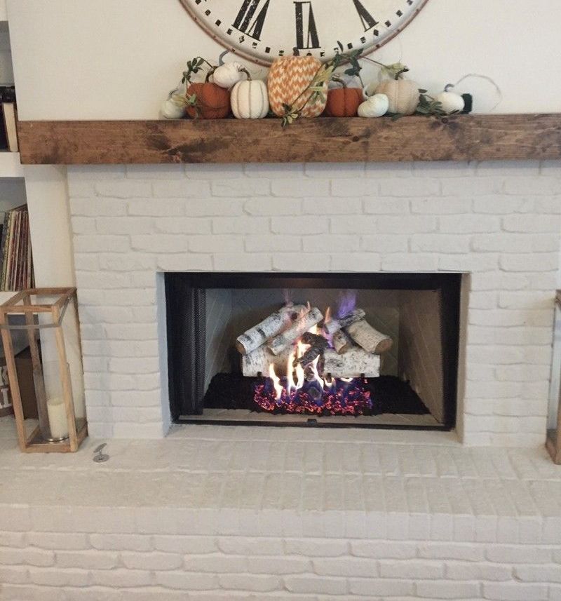 A fireplace with a clock above it and pumpkins on the mantle