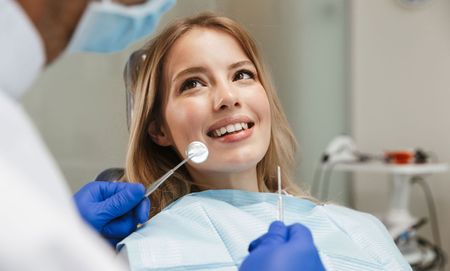 A woman is sitting in a dental chair while a dentist examines her teeth.