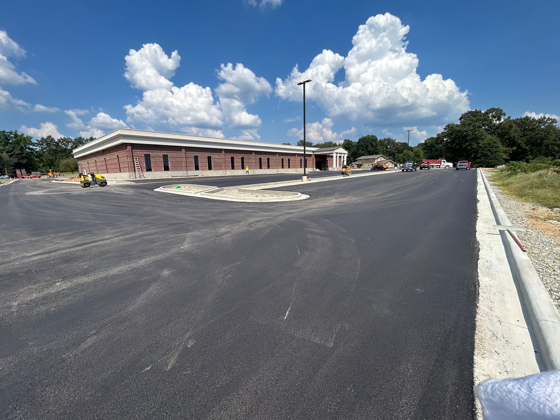 Wide asphalt lot beside a low brick building under a bright blue sky with large white clouds