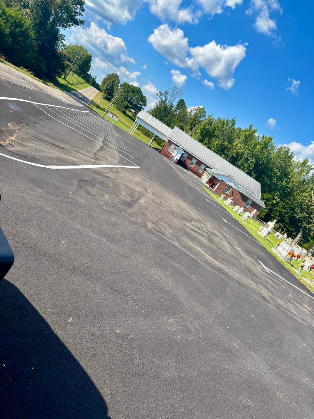 Empty parking lot with a white building and trees under a bright blue sky with clouds