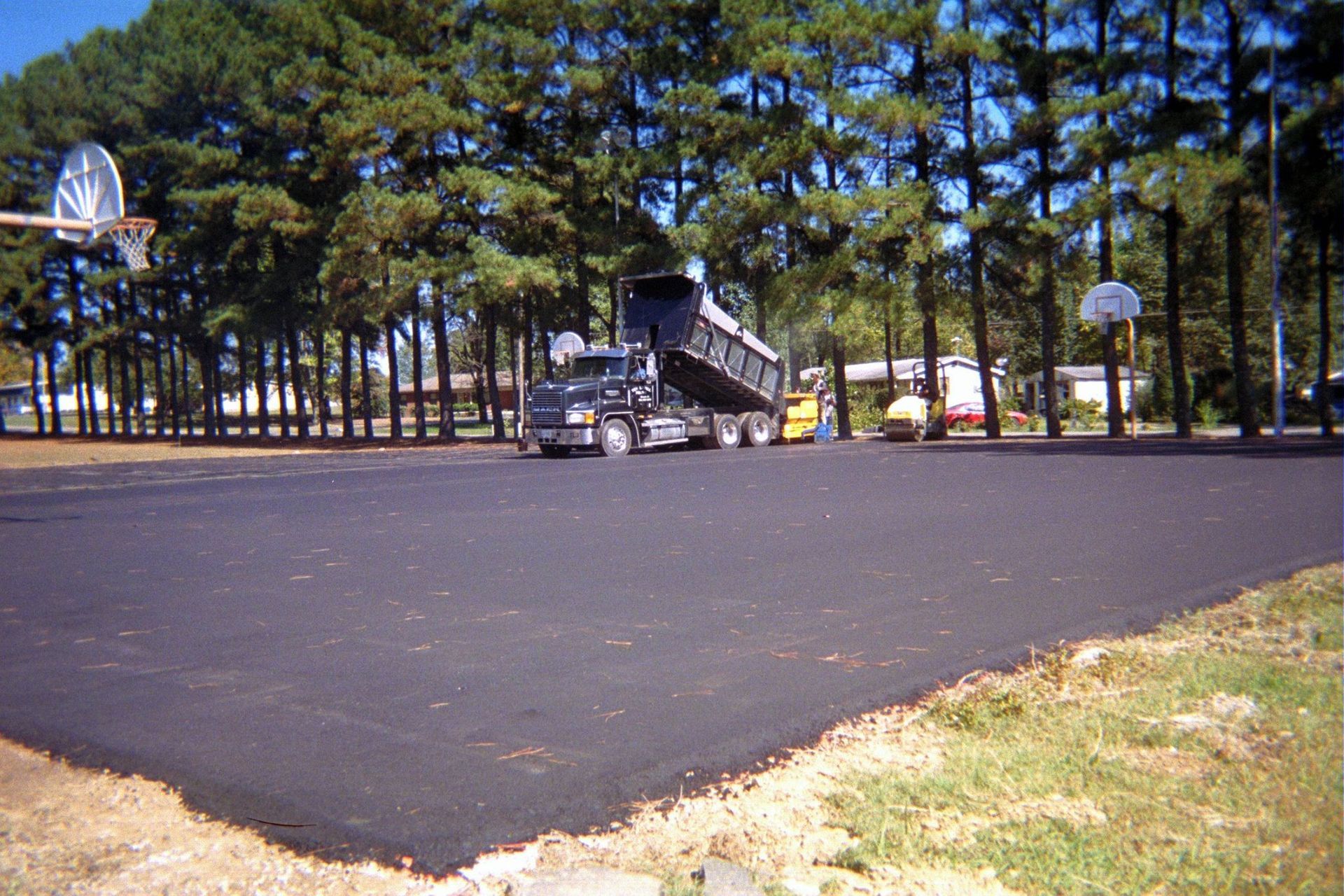Empty asphalt lot with a parked black truck, trees, and basketball hoops in the background