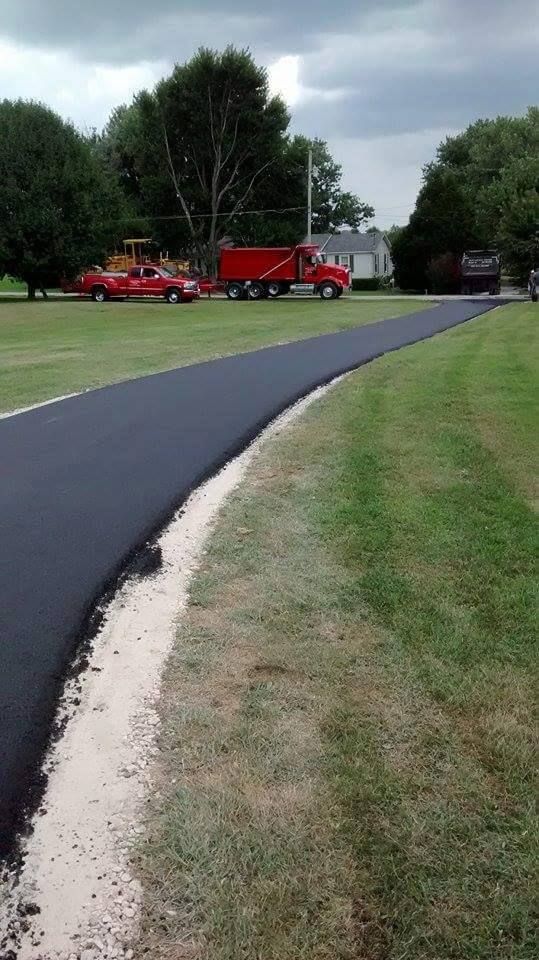 Freshly paved black road curving through a grassy park with red utility trucks parked near trees