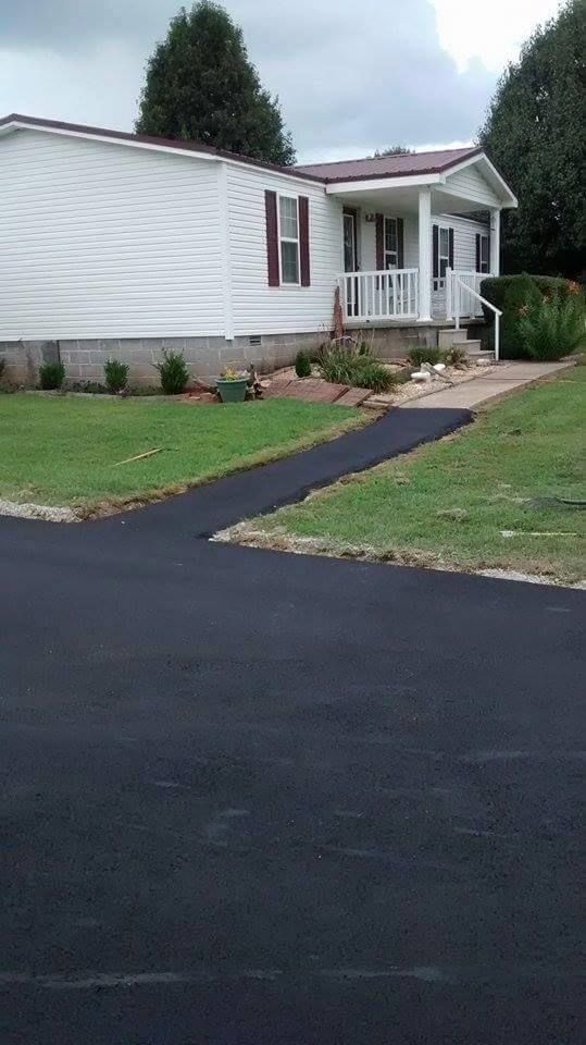 Single-story white house with a small porch, front lawn, and dark paved driveway.
