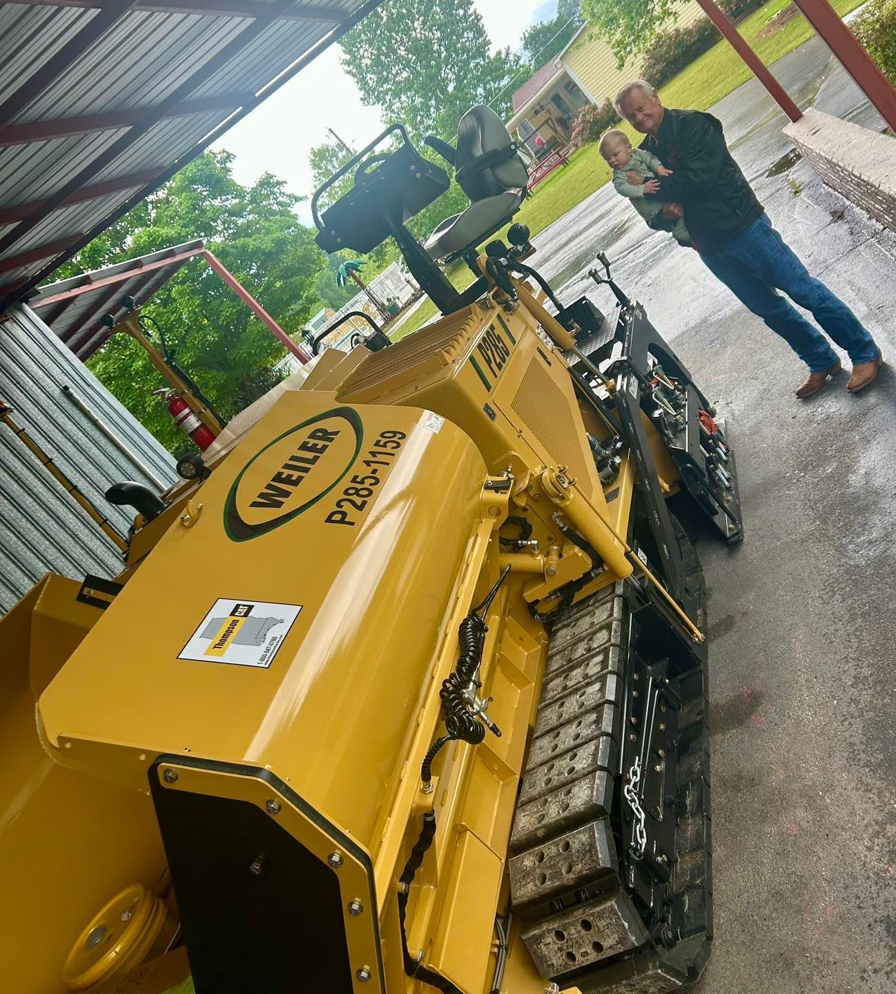Yellow tracked construction machine beside a person in a covered outdoor work area