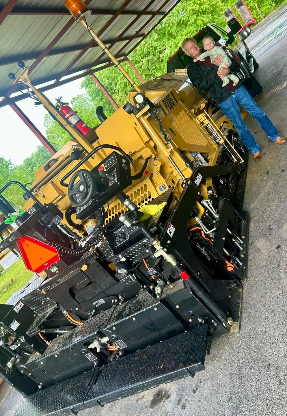 Yellow industrial machine displayed indoors with two people standing beside it under a metal-roofed shelter