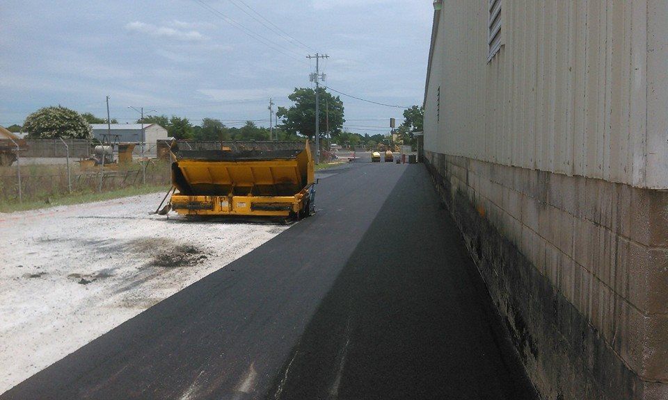 Yellow road paver on a newly paved roadside beside a large building
