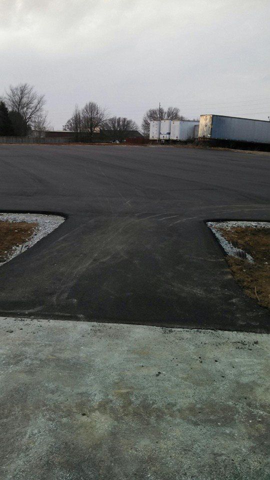 Empty paved lot with a few trees and parked trucks under a gray overcast sky