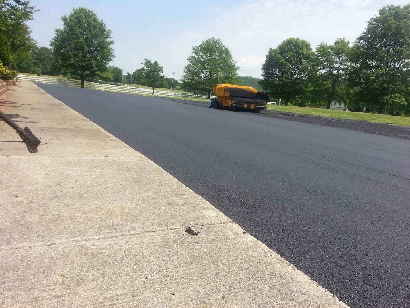 Newly paved road with a yellow truck on the right side and trees along the roadside