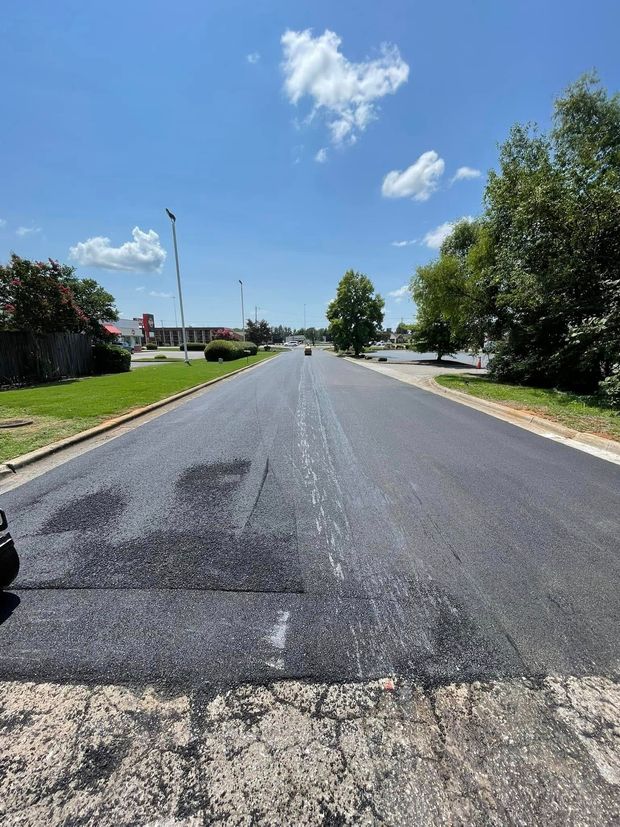 Freshly paved road stretching into a sunny residential area under a blue sky with clouds