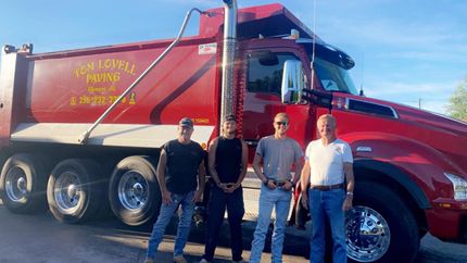 Three people standing beside a red dump truck on a sunny day