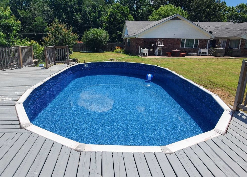 A large swimming pool is sitting on top of a wooden deck in front of a house.