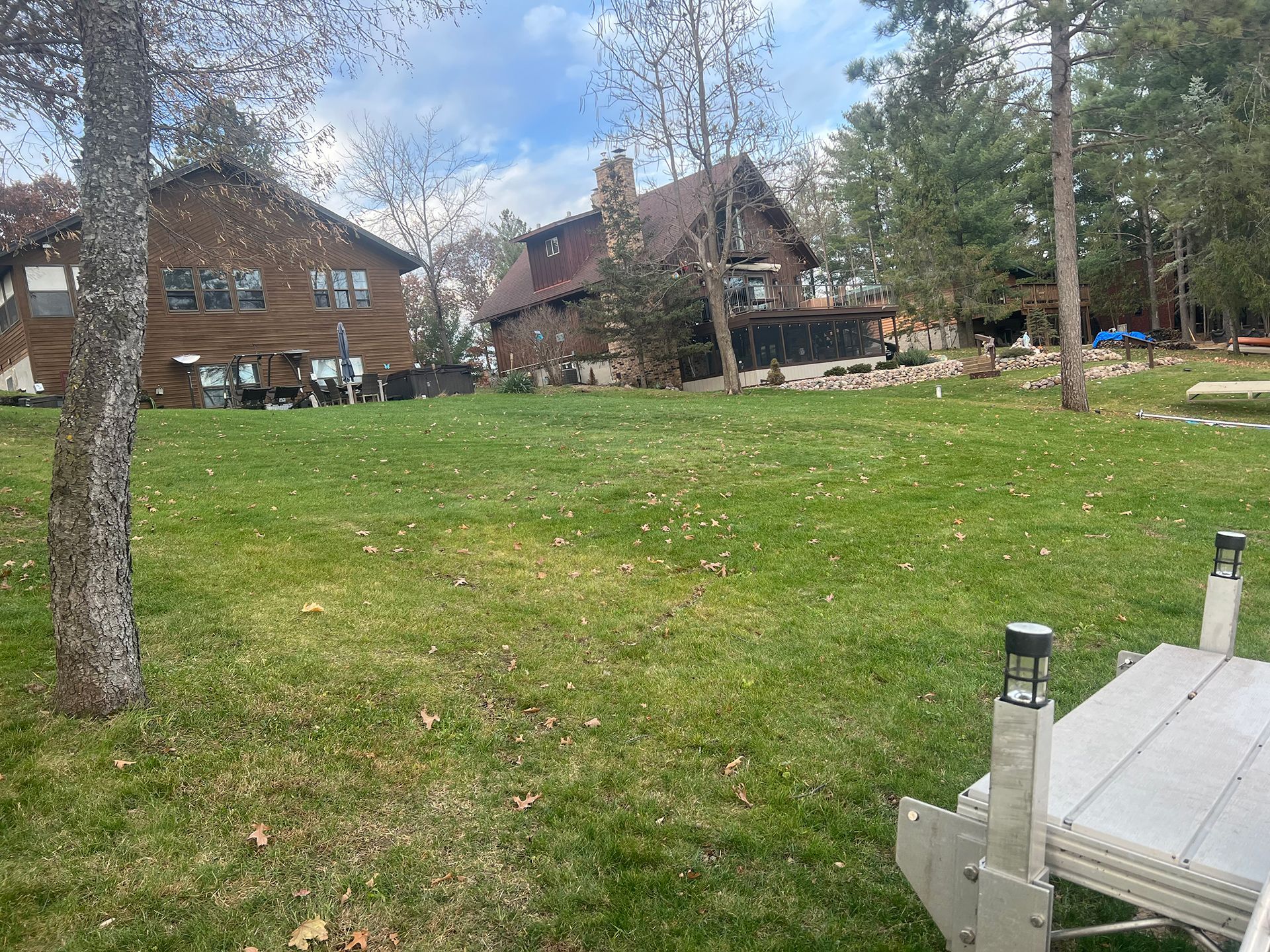 A large grassy field with a dock in the foreground and a house in the background.