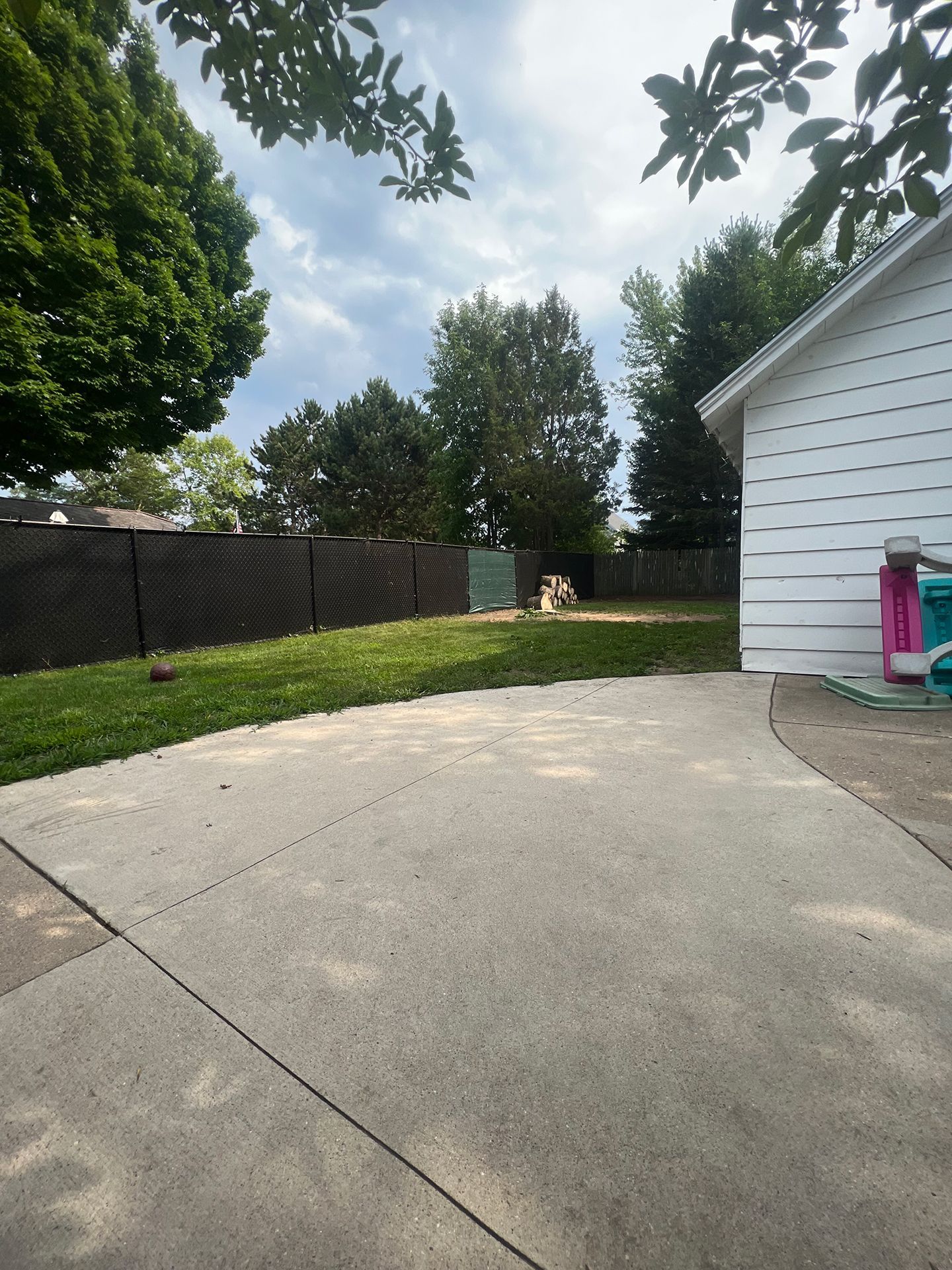 A concrete driveway leading to a house with a fence in the background