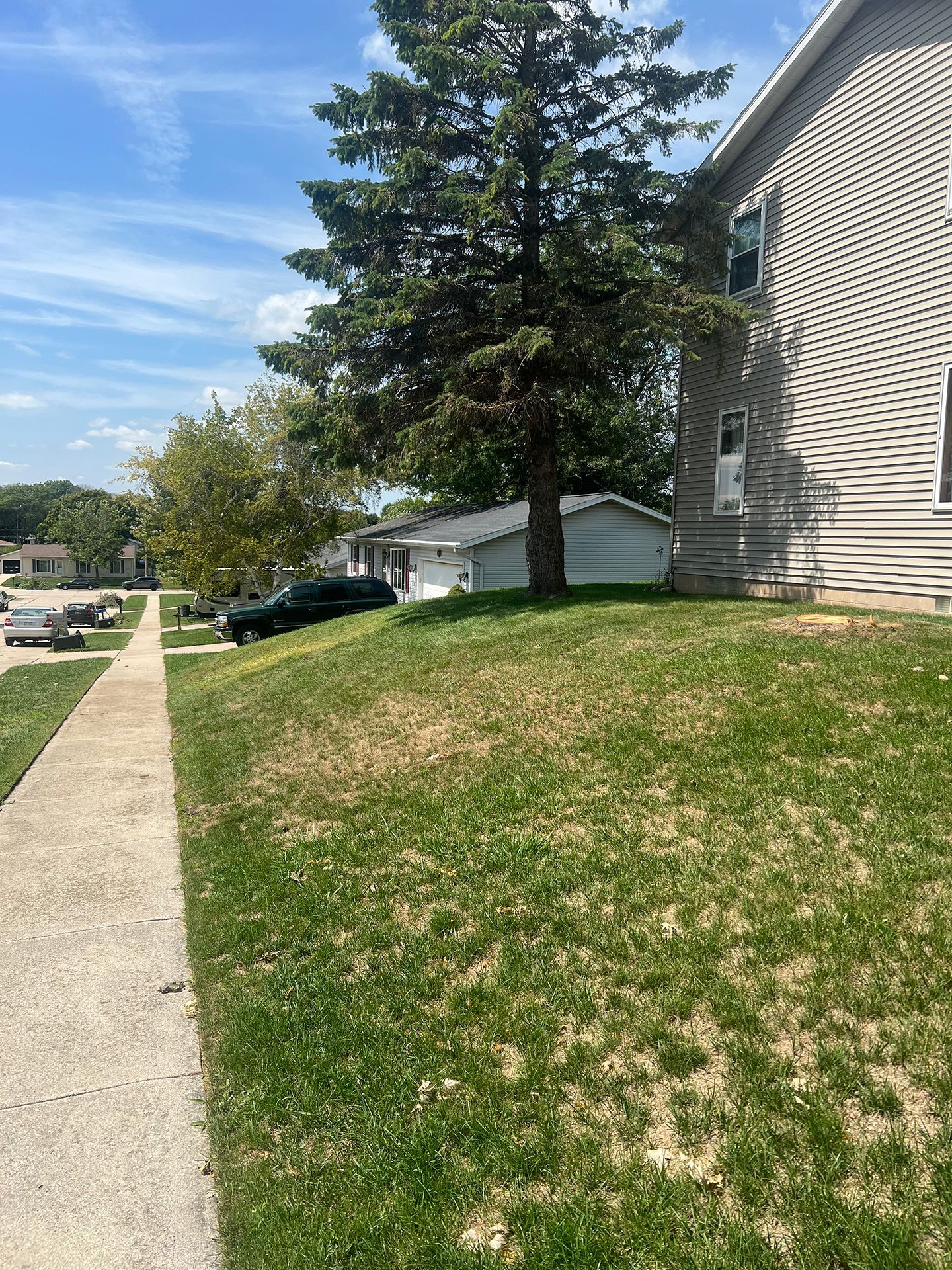 A house is sitting on top of a grassy hill next to a sidewalk.
