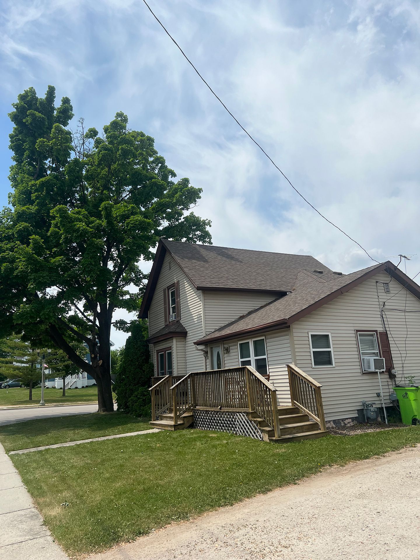 A white house with a wooden deck and stairs in front of it.