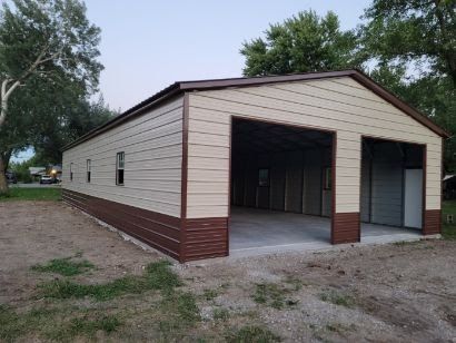 A large metal garage with two doors is sitting in the middle of a dirt field.