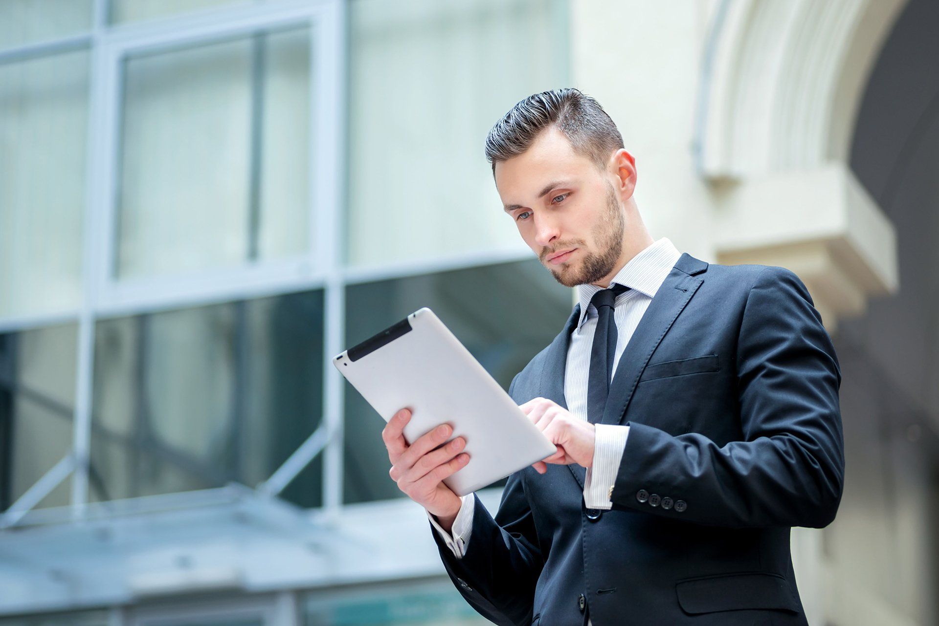 Man in suit looking at tablet in front of a modern building.