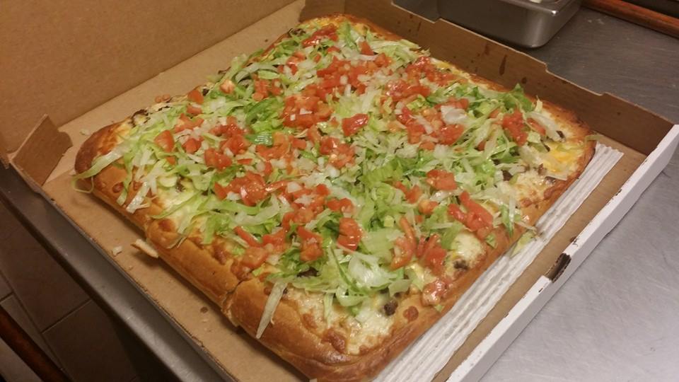 A pizza with lettuce , tomatoes and cheese is in a cardboard box.